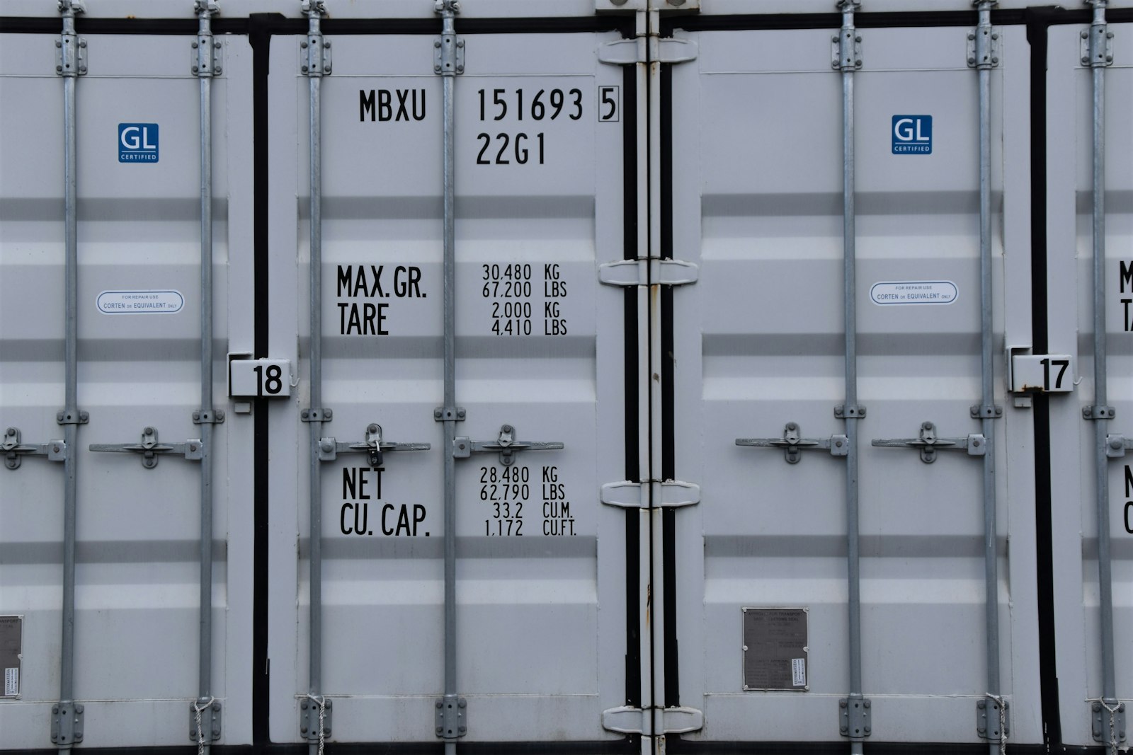 Head-on view of a grey shipping container's rear doors showing the four vertical locking bars, cam keepers, and hasp hardware that RMA Fleet compares against storage trailer door security