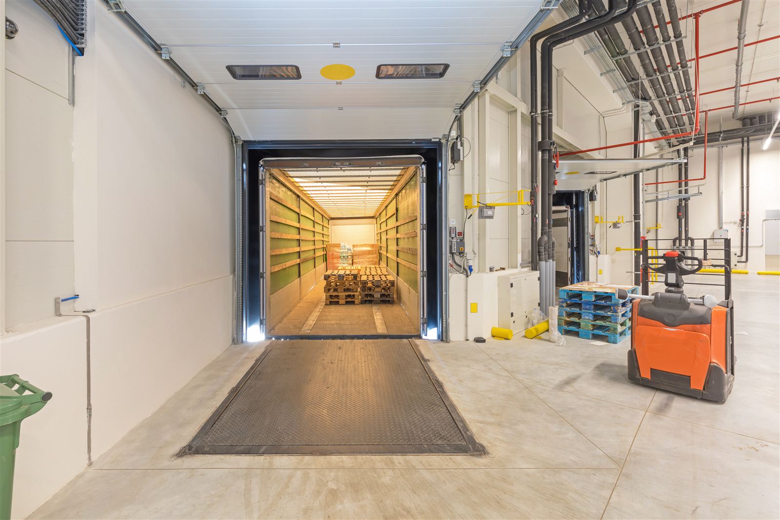 Dock height loading in action: open storage trailer at a warehouse dock door with the dock plate down and a pallet mover staged nearby