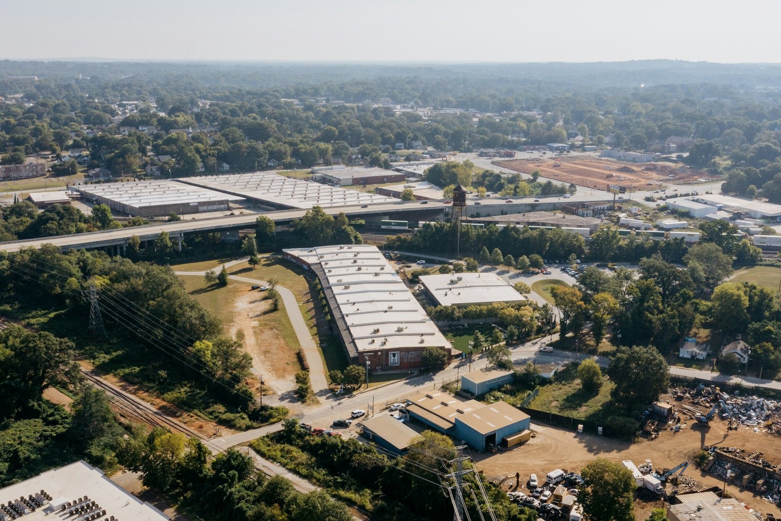 Aerial view of a Midwest industrial district with warehouse buildings, a highway overpass and rail lines, the kind of short lane RMA Fleet runs dock to dock delivery and scheduled shuttle routes across