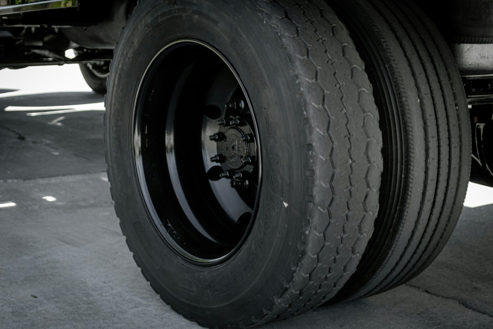 Ground level close up of a heavy truck wheel and dual tires on a steel rim bearing load on a concrete lot, the running gear that carries a loaded 53 foot trailer