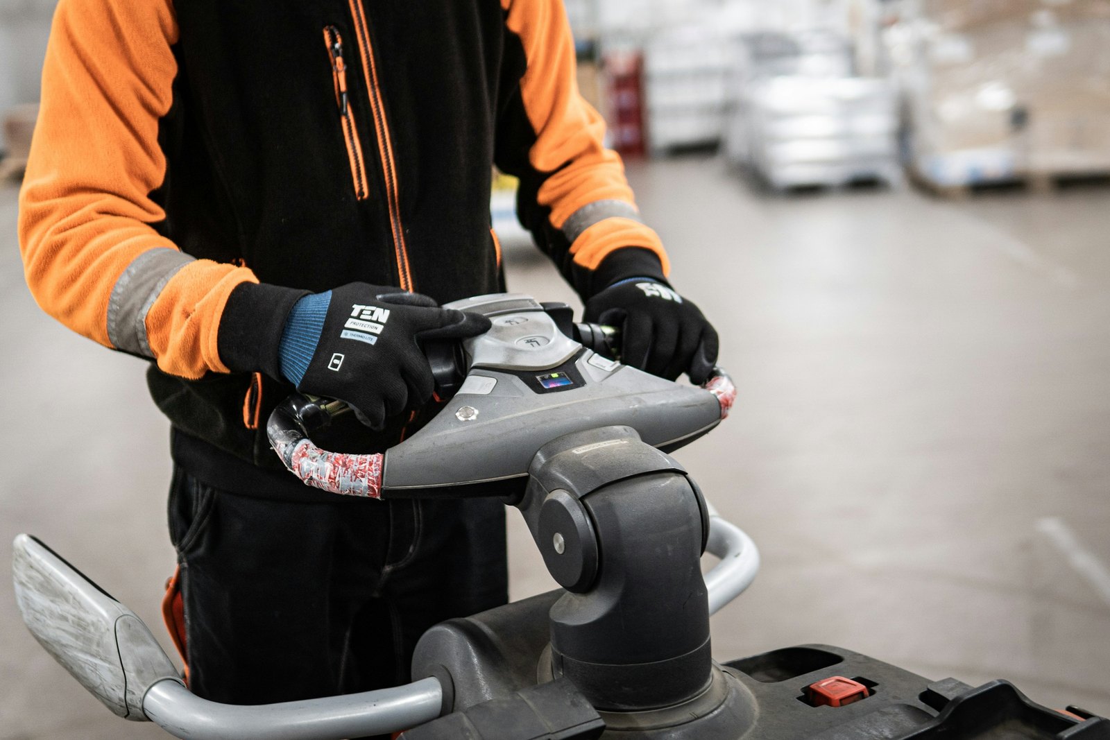 Warehouse worker in high visibility sleeves steering an electric pallet jack past staged pallets, the kind of dock work that has to finish before RMA Fleet picks up a same day freight load