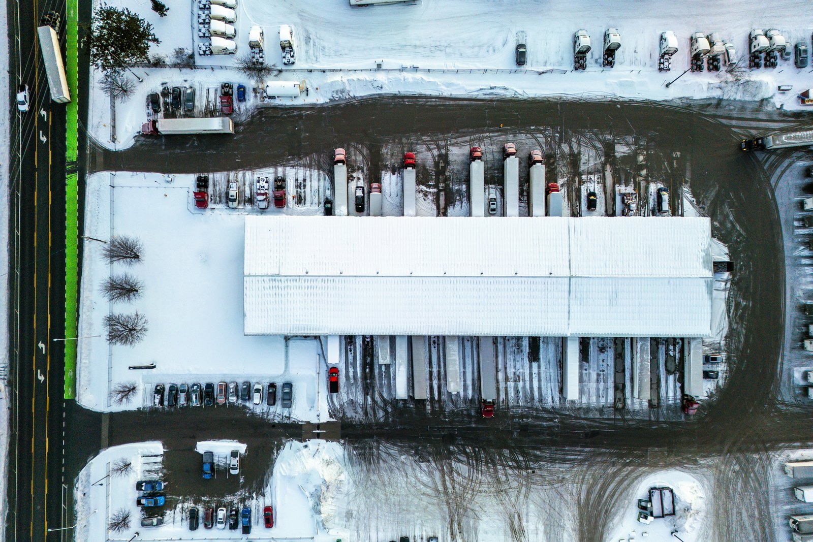 Overhead view of a snow covered cross dock terminal with dry van storage trailers backed into the dock doors and plowed lanes between them, the winter conditions RMA Fleet storage trailers sit in across the Cincinnati Tri-State